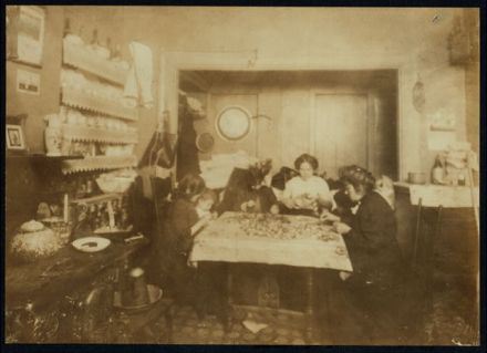 2 P.M. Mrs. Katie --- (refused to give their name), 134 1/3 Thompson St., one flight up, front. Making artificial flowers in a crowded and dirty room used as kitchen, bed room, living room, and work room. Mother and family work including 8 and 9 yr. old girls in the photo (who were at home 2 P.M. on a school day) and the little 3 and 4 yr. olds who were helping by separating the petals. See report on schedule. Name is Darelli [or Tarelli?] 3 days after photo was taken the home was sealed up and disinfected by Board of Health for tuberculosis; 14 yr. old boy. Immediately the flower making resumed again. Location: New York, New York (State)