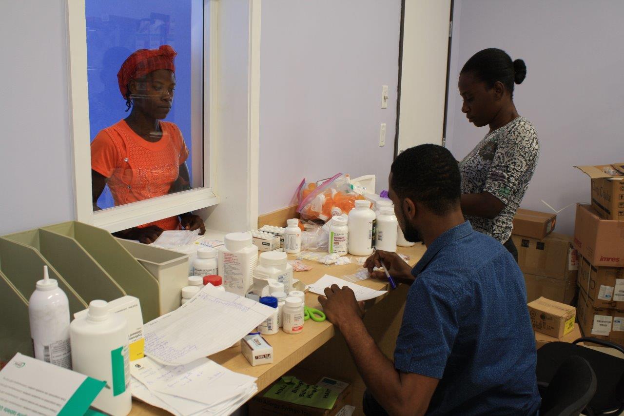 A patient at the hospital picks up her medication from Demar and Darcelin Jean at the pharmacy. (1)